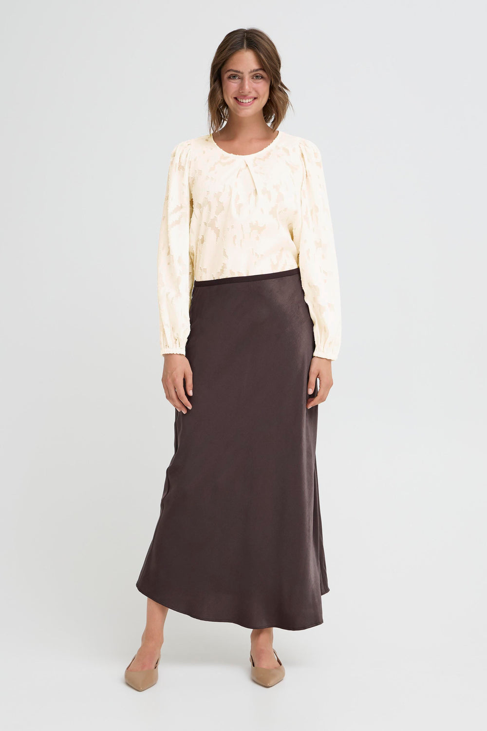 Woman wearing a cream blouse and brown skirt on a white background