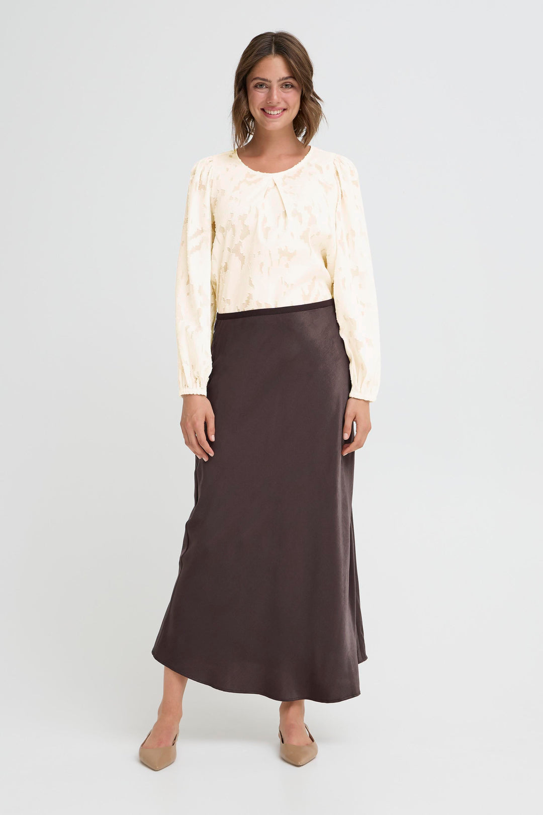 Woman wearing a cream blouse and brown skirt on a white background