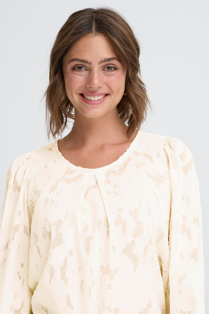 Woman wearing a light-colored textured top against a plain background