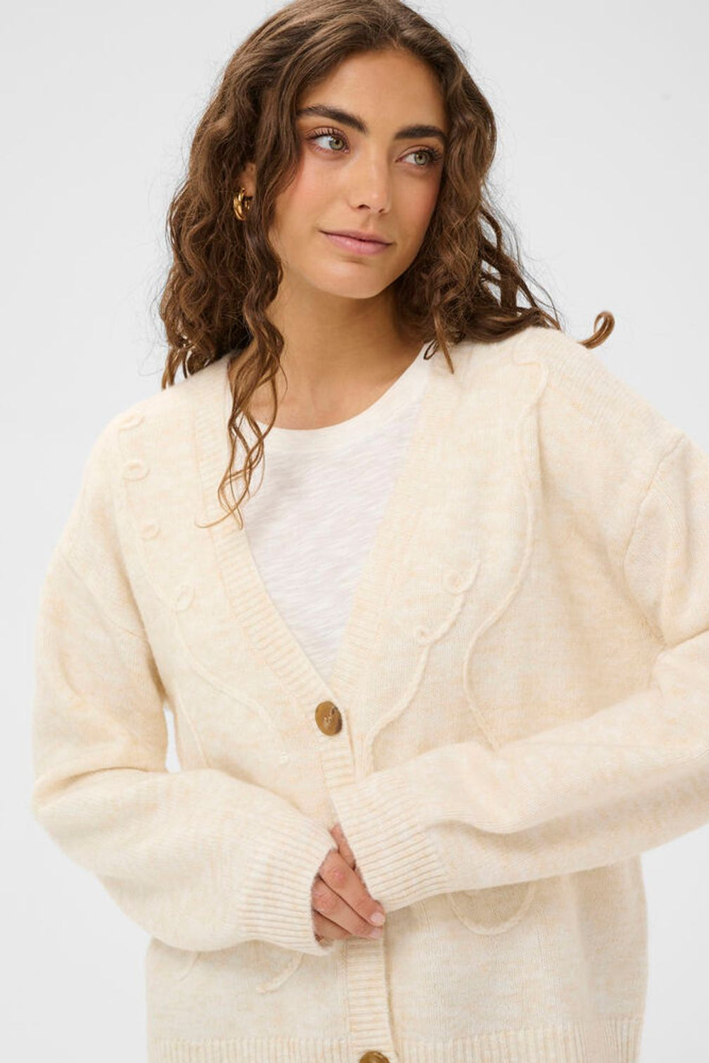 Woman wearing a cream cardigan over a white shirt on a light gray background