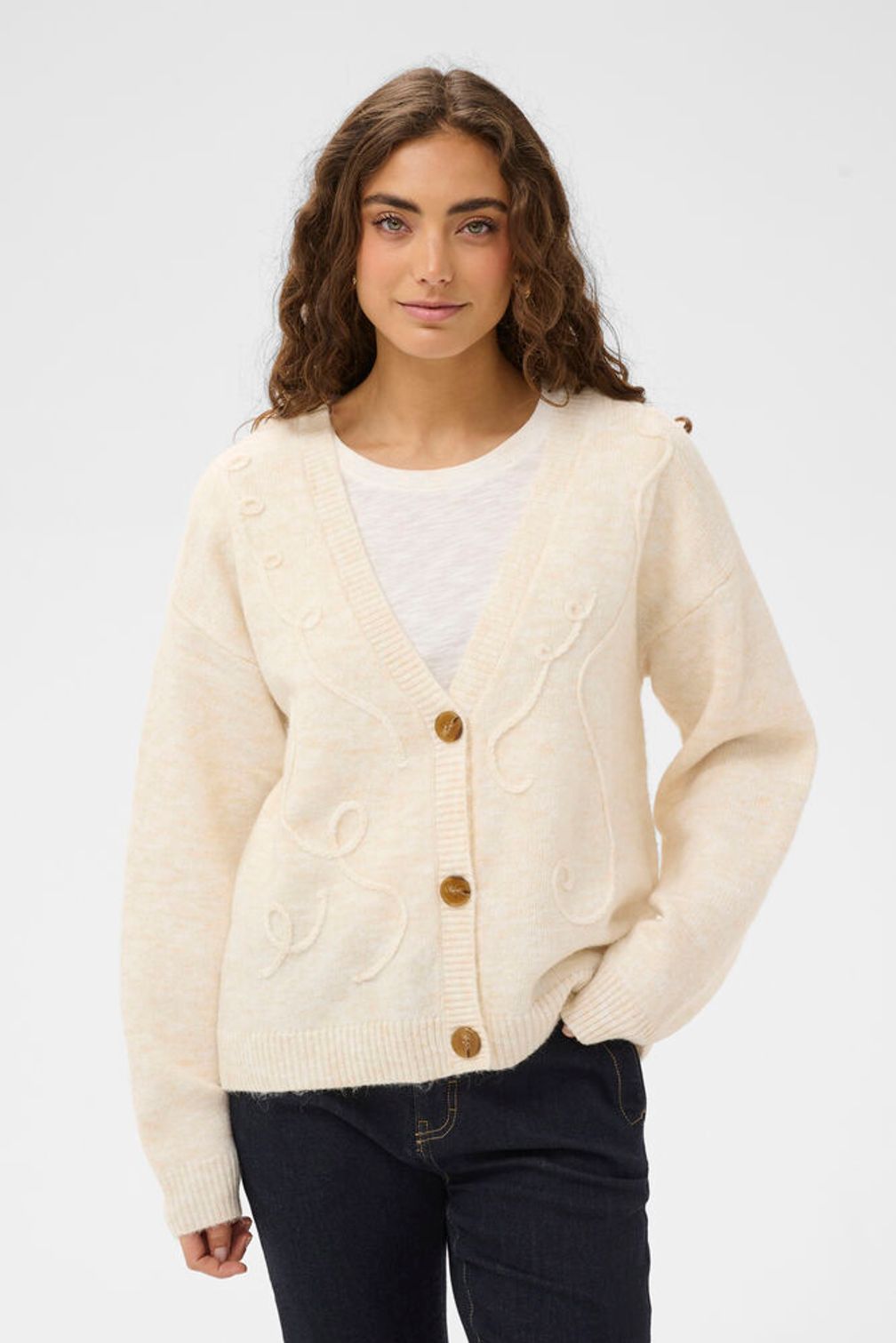 Woman wearing a cream cardigan over a white shirt on a light gray background