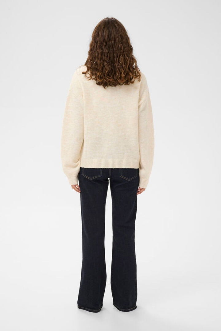 Person wearing a cream sweater and black pants on a white background