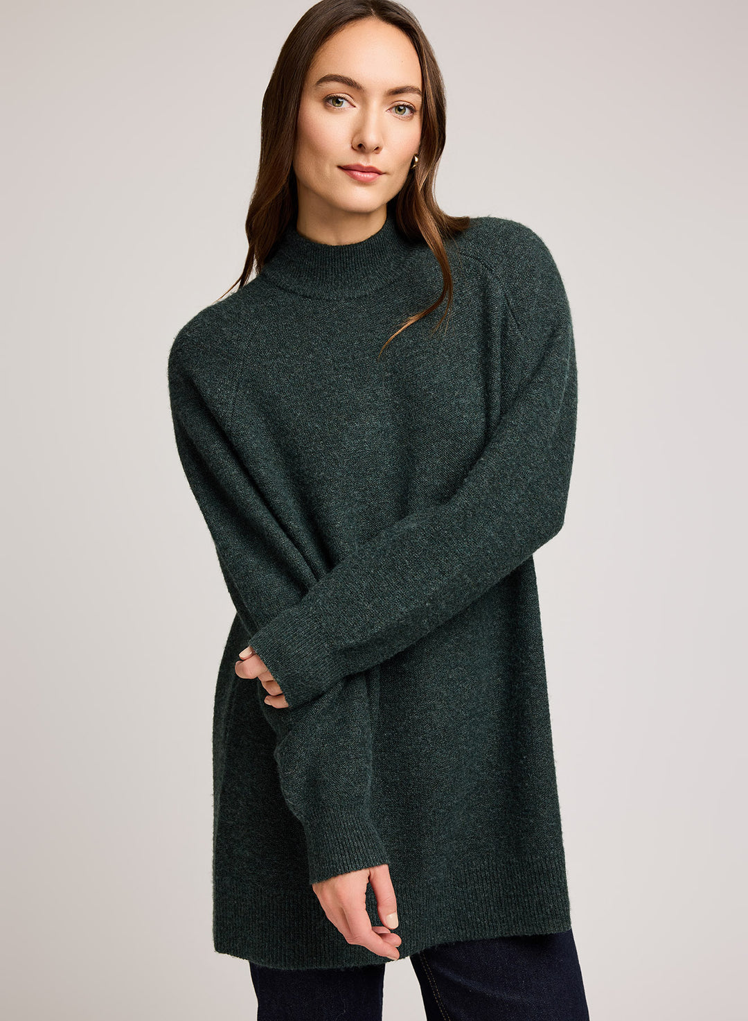 Woman wearing a dark greent tunic knit sweater against a plain background