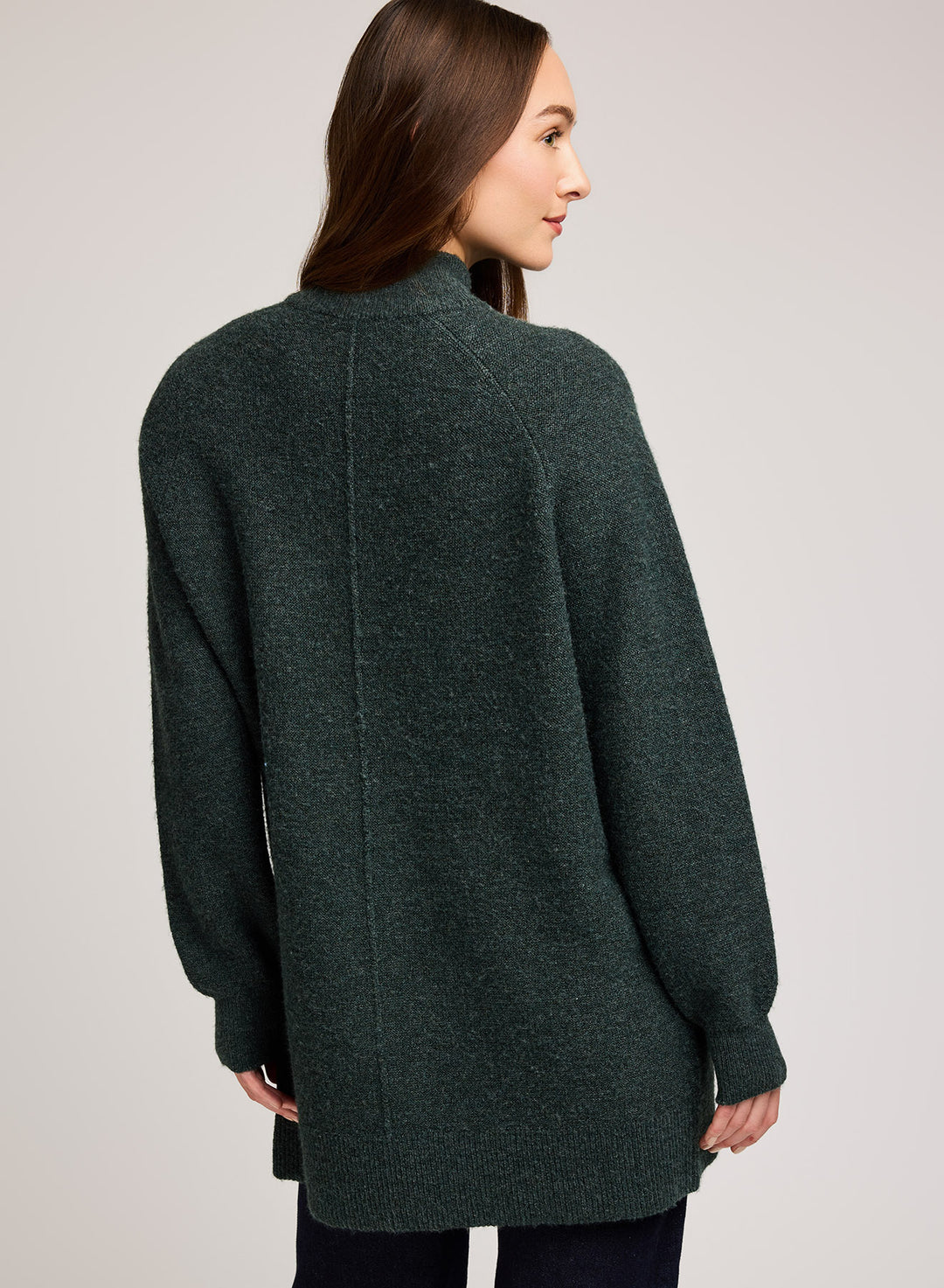 Woman wearing a dark green sweater against a plain background