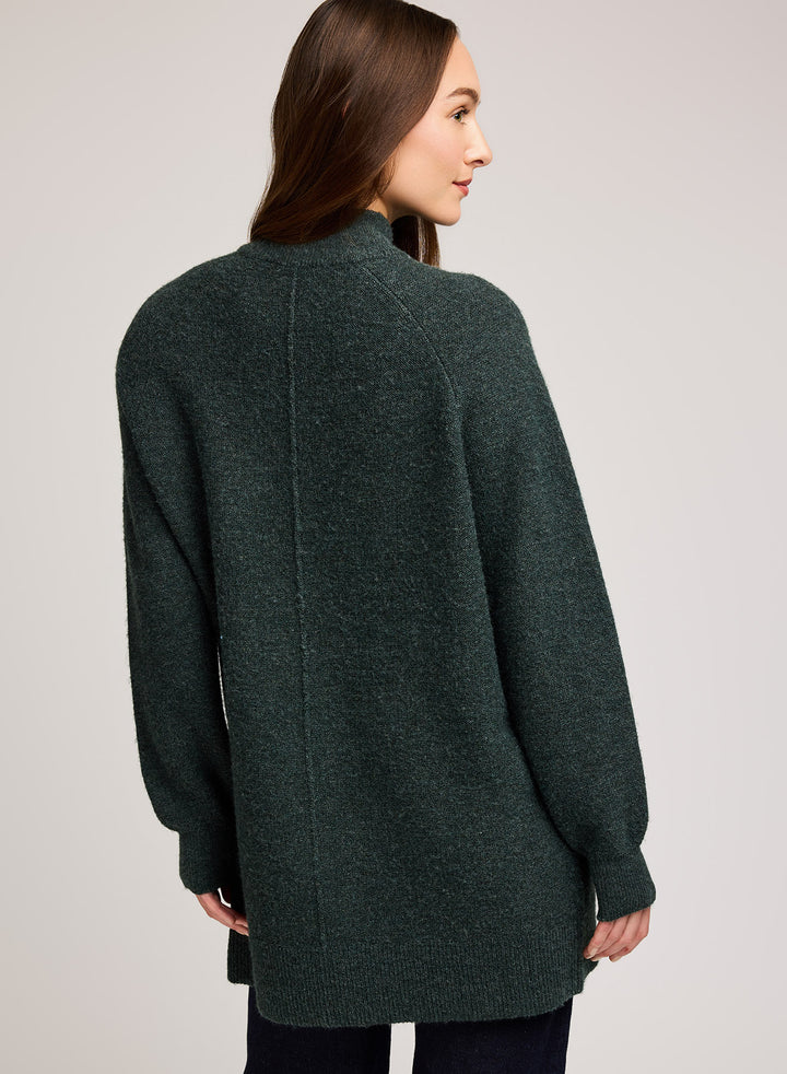 Woman wearing a dark green sweater against a plain background