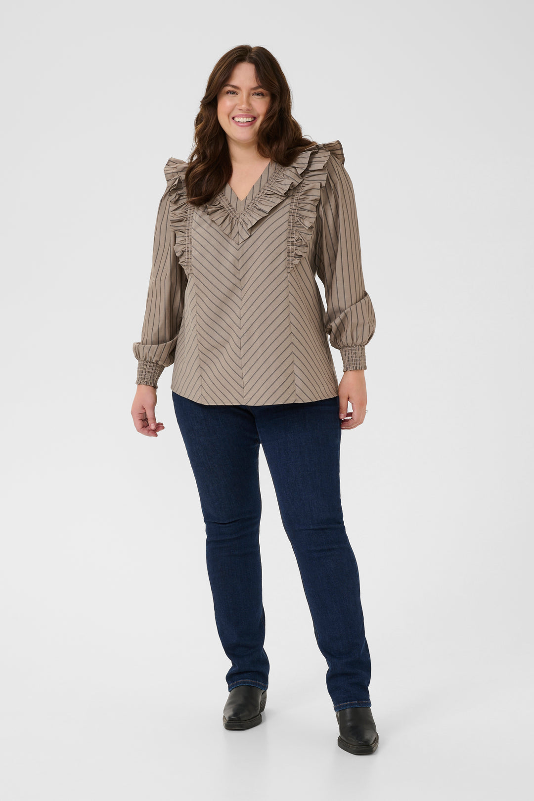 Woman wearing a patterned blouse and dark jeans on a white background