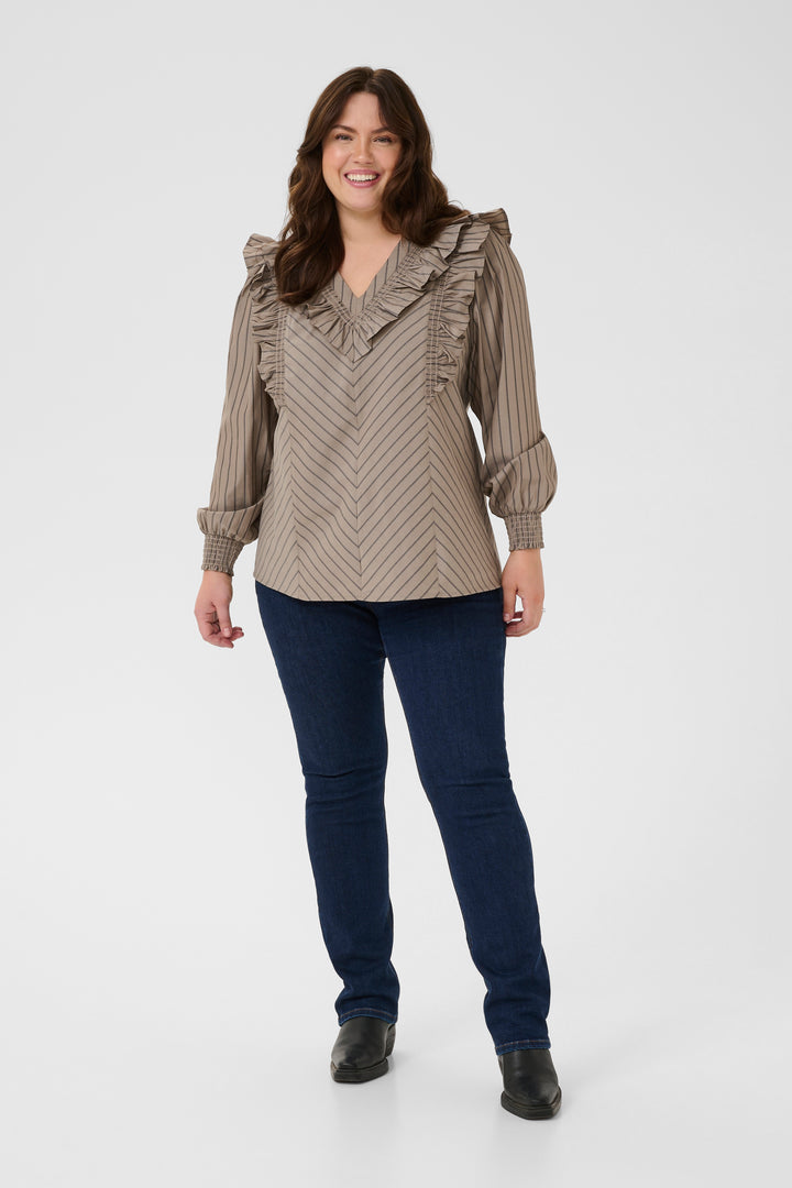 Woman wearing a patterned blouse and dark jeans on a white background