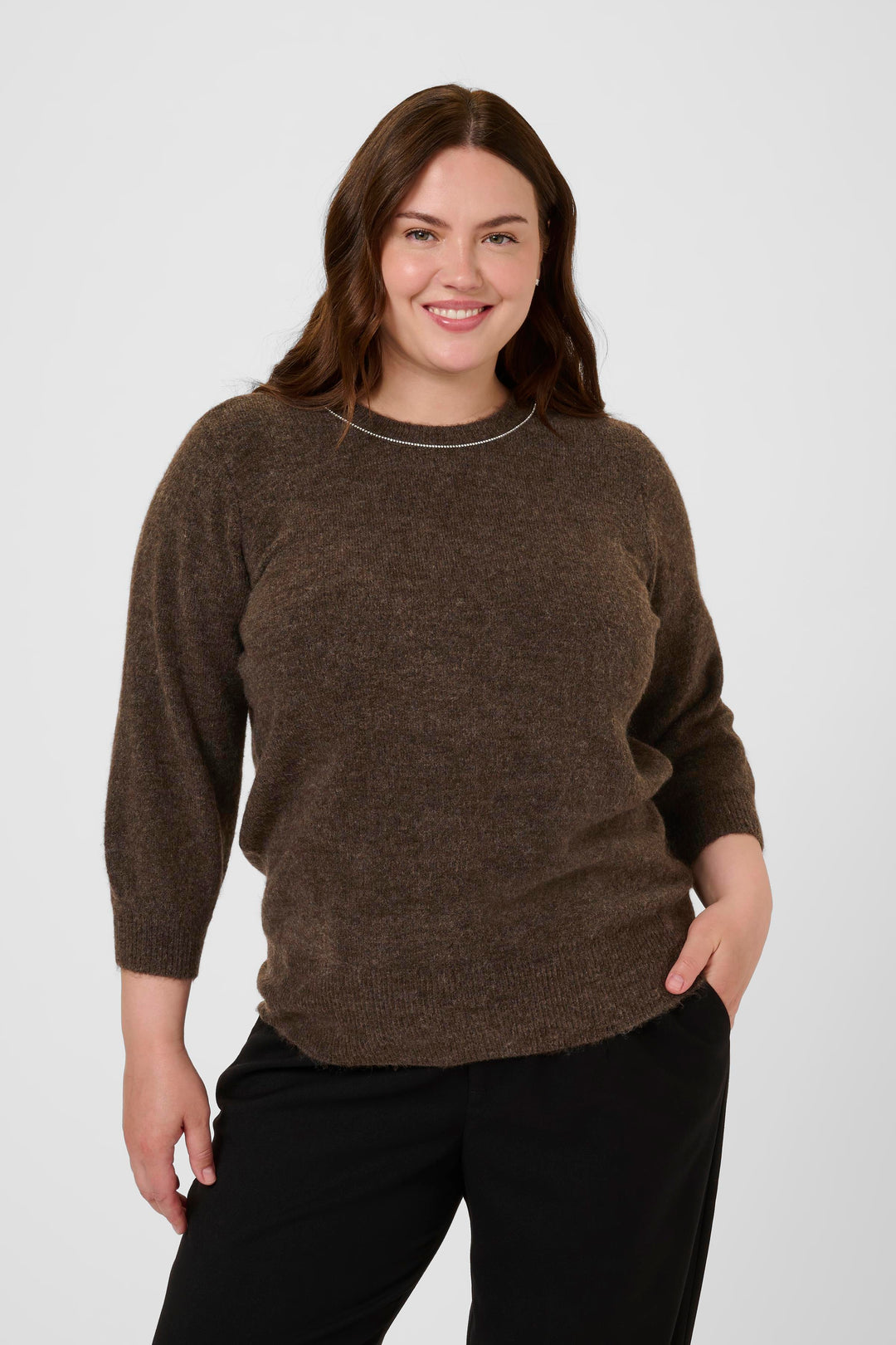 Woman wearing a brown sweater and black pants against a white background