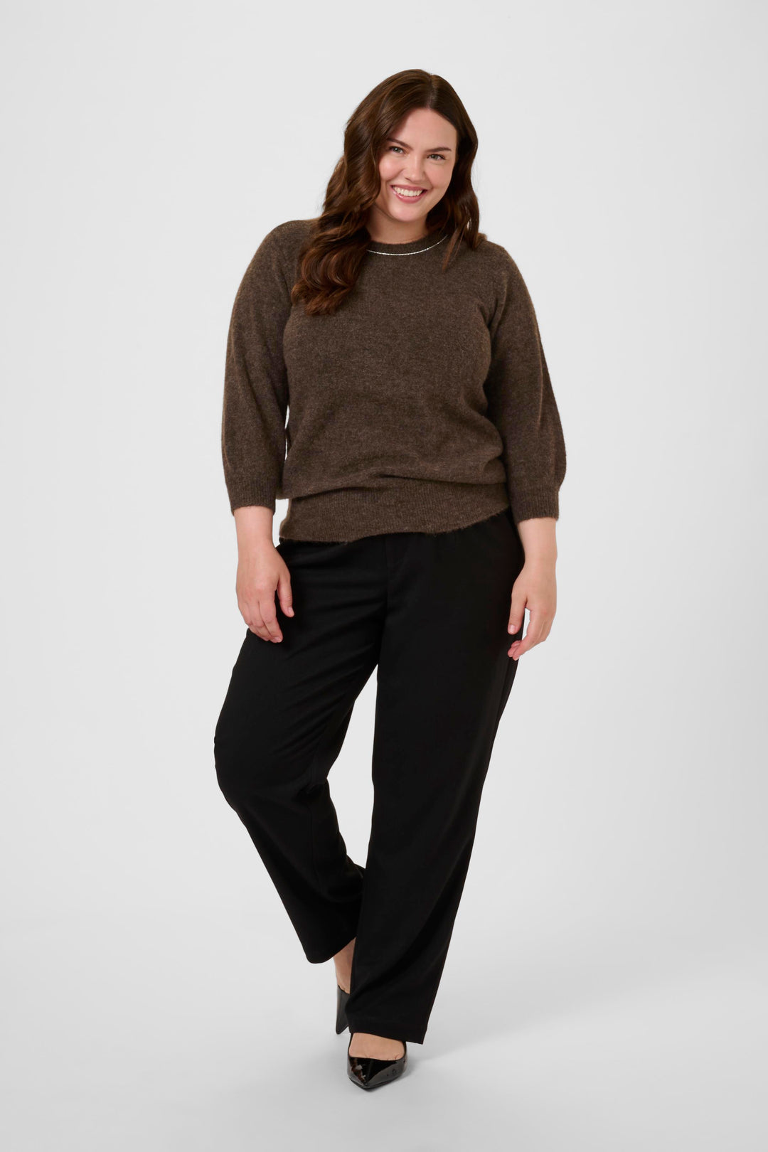 Woman wearing a brown sweater and black pants on a white background