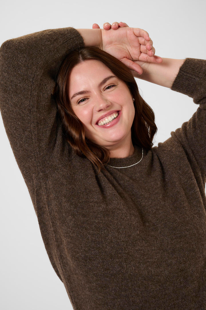 Woman wearing a brown sweater with her arms raised against a white background