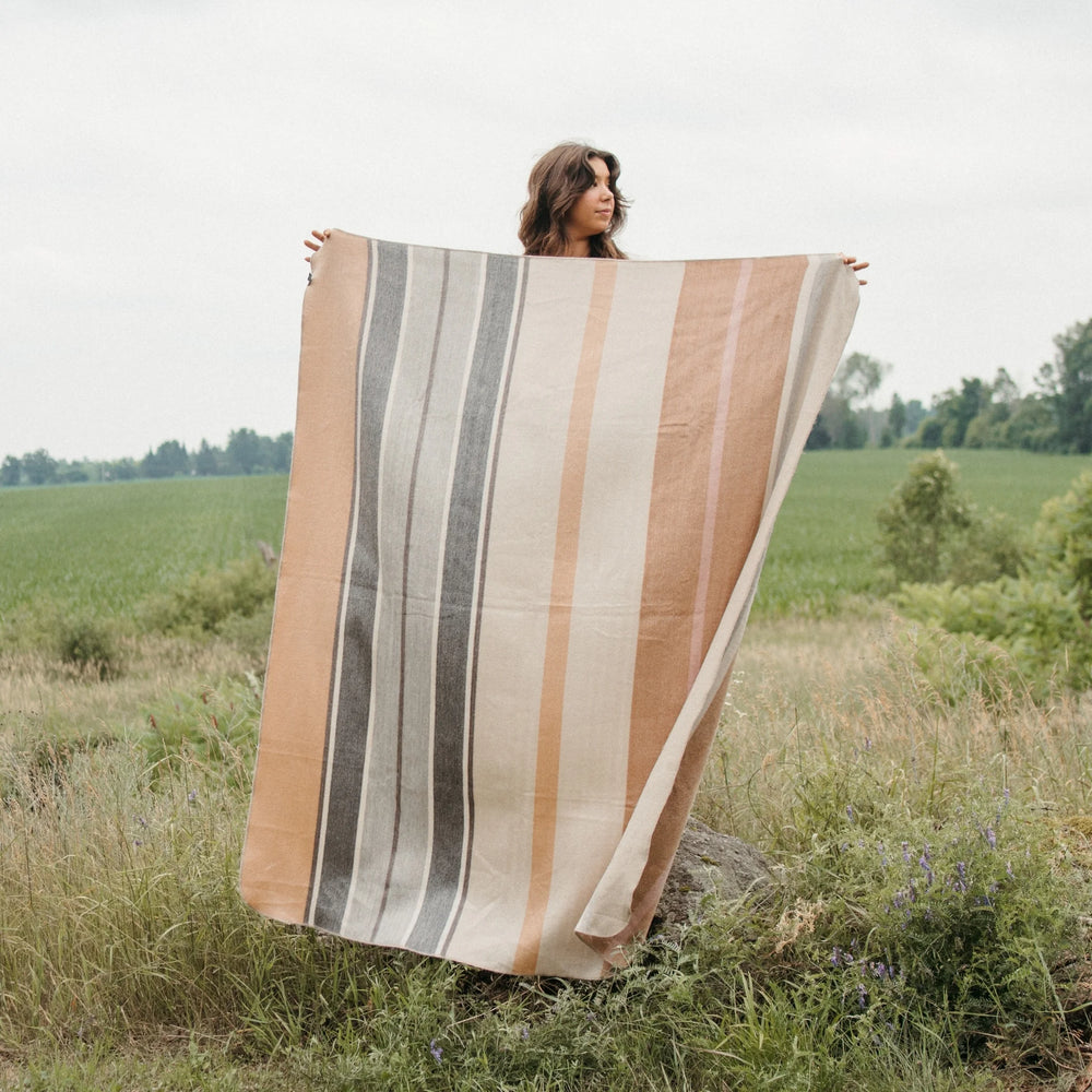 Person holding a alpaca wool blanket with beige and grey striped pattern in a field