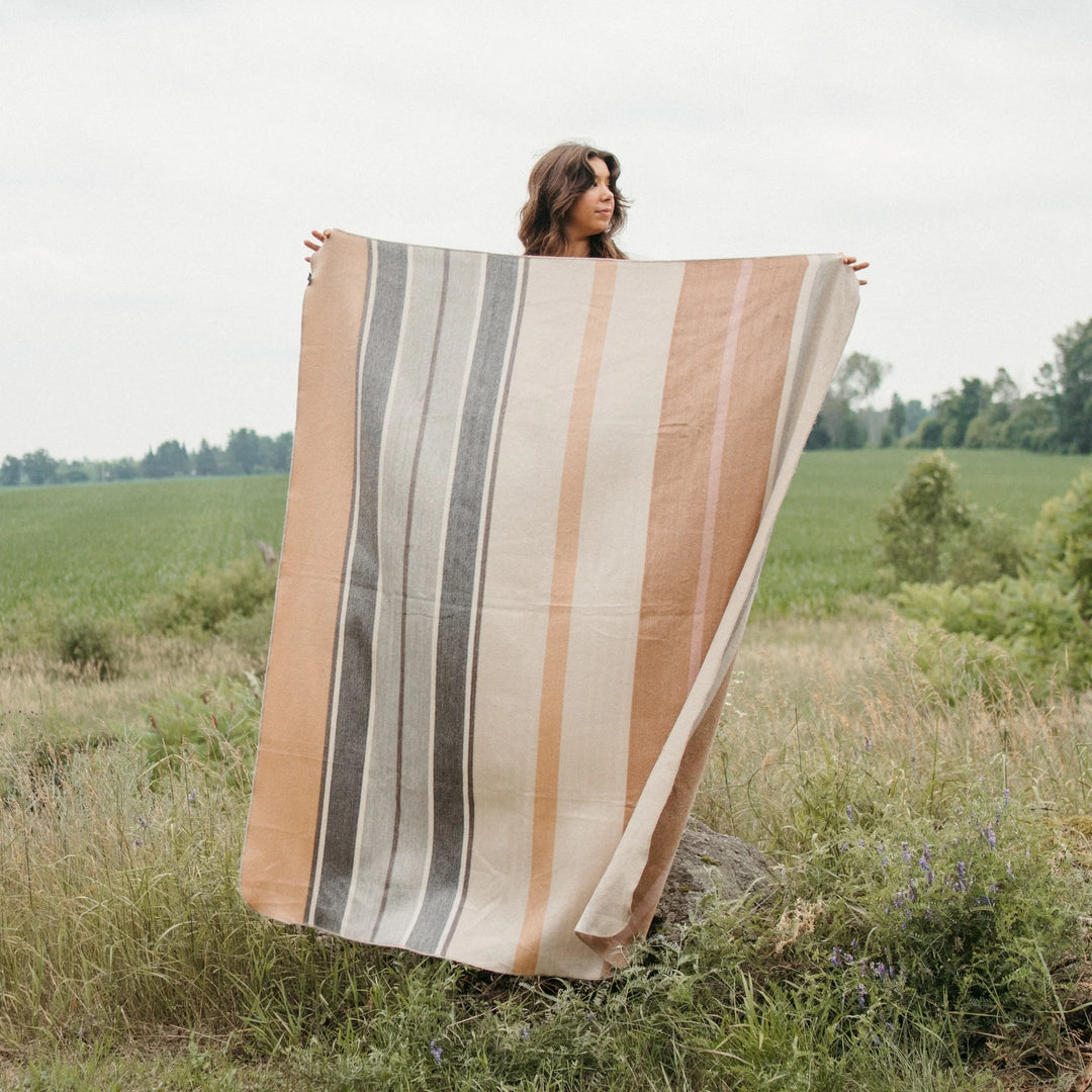 Person holding a alpaca wool blanket with beige and grey striped pattern in a field