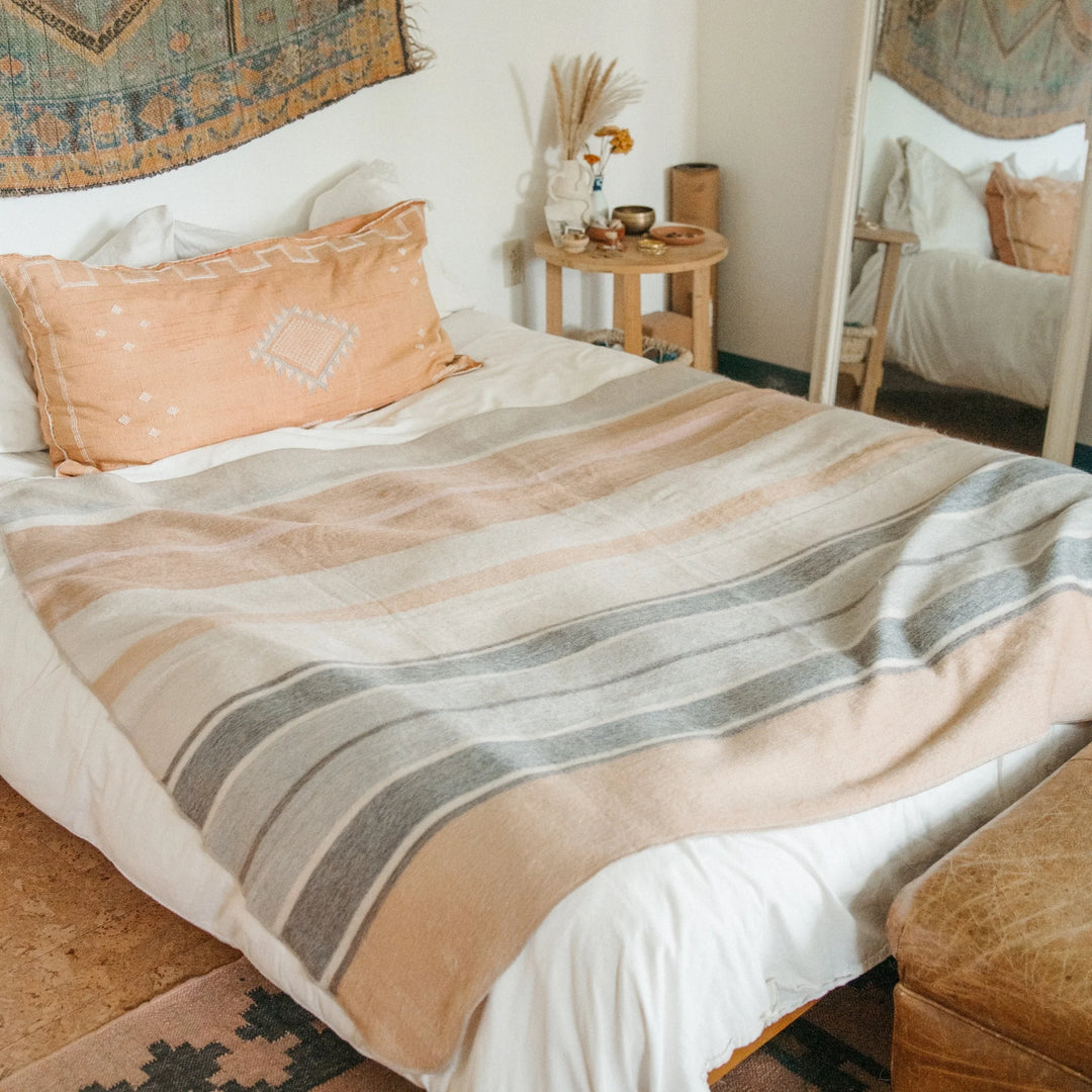 Bed with an alpaca wool blanket with beige and grey striped pattern  in a cozy bedroom setting.