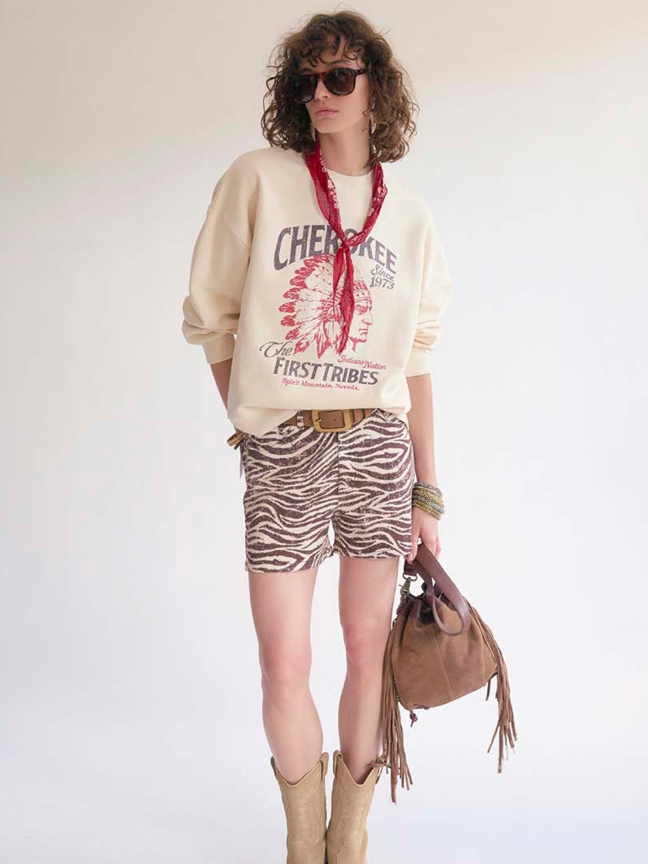 Person wearing a beige sweater with a graphic design, zebra print shorts, and tan boots on a white background.
