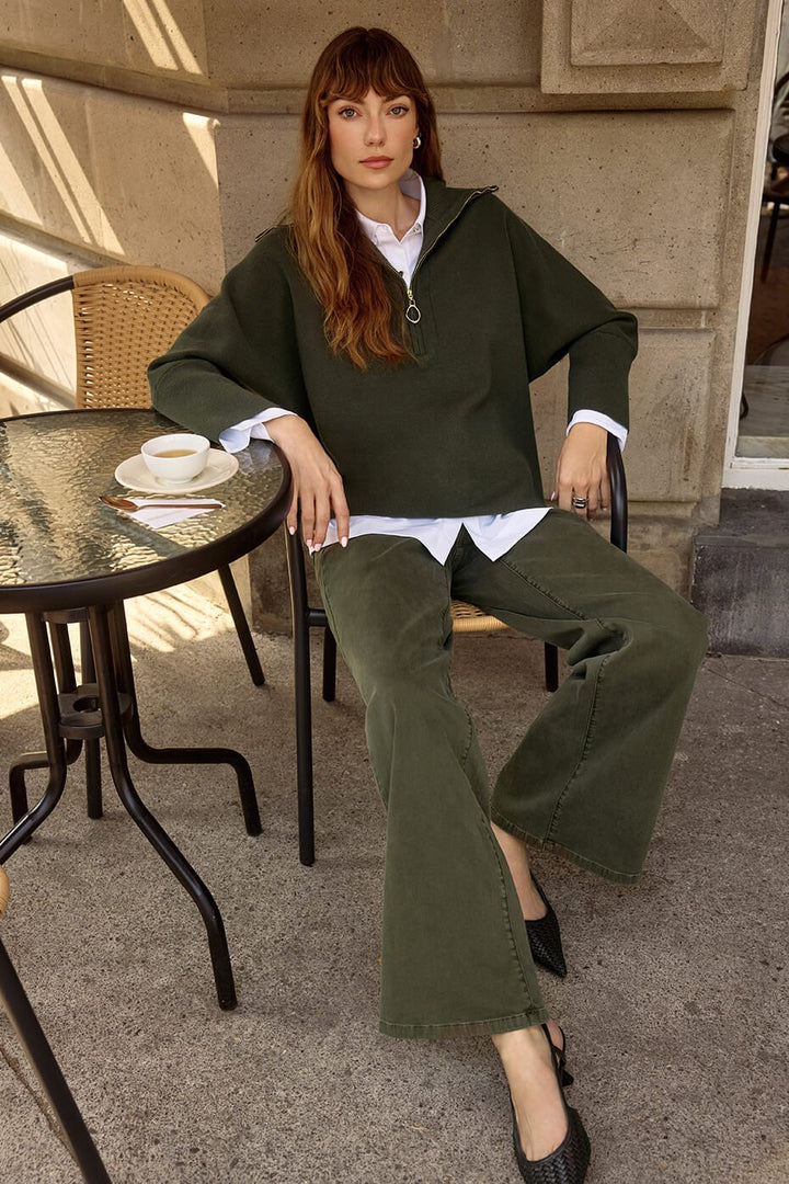 Woman sitting at an outdoor cafe table wearing a green sweater and green pants.
