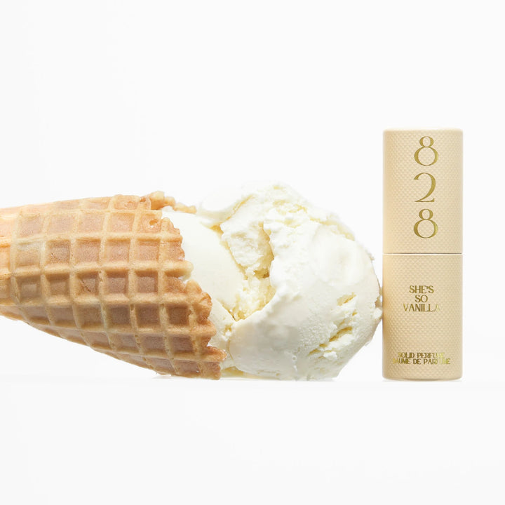 Ice cream cone with vanilla ice cream next to a perfume bottle labeled '828 She's So Vanilla' on a white background