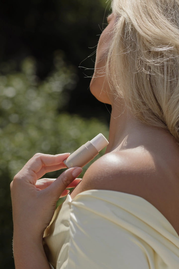 Woman applying vanilla_Solid_pefume_stick to her shoulder outdoors