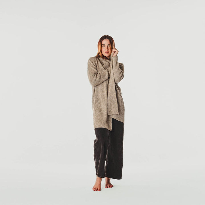 Woman wearing a beige sweater and black pants on a white background