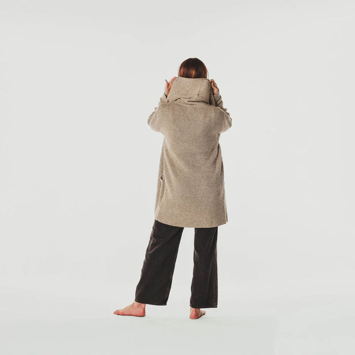 Person wearing a beige coat and black pants on a white background