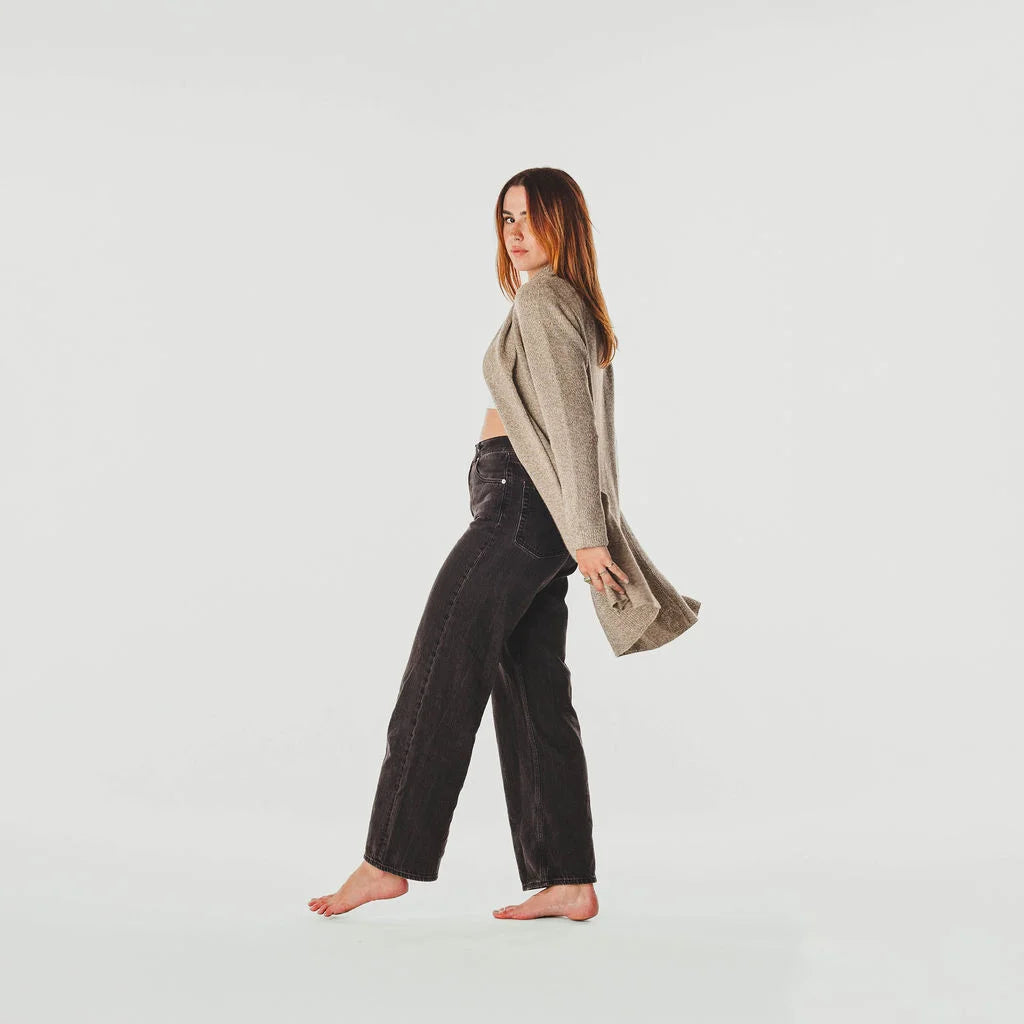Woman wearing a beige cardigan and dark pants on a light gray background