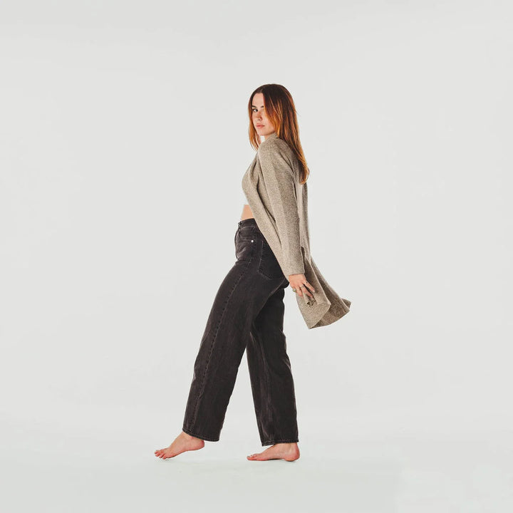 Woman wearing a beige cardigan and dark pants on a light gray background