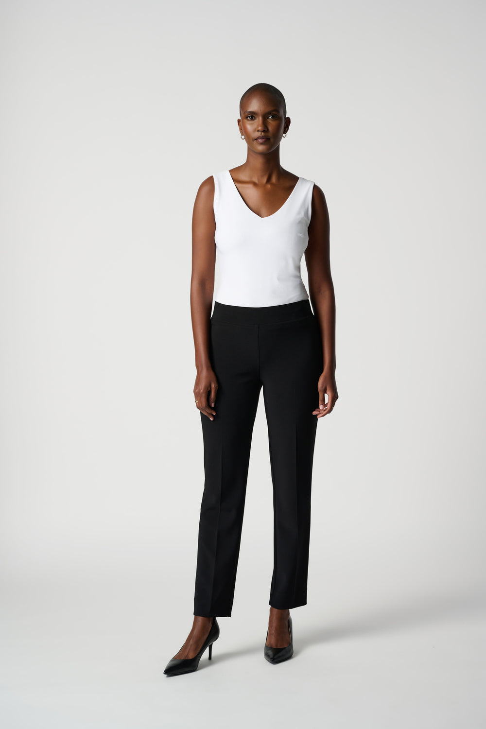 Woman wearing a white sleeveless top and black pants on a white background