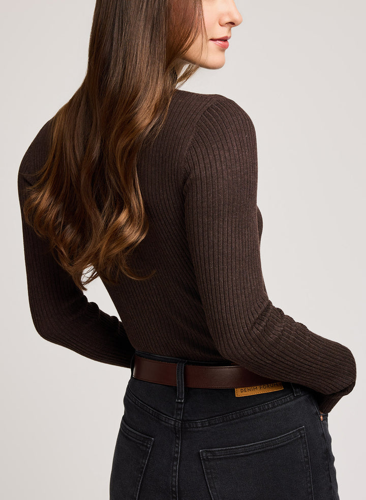 Person wearing a brown ribbed sweater and dark jeans on a light gray background