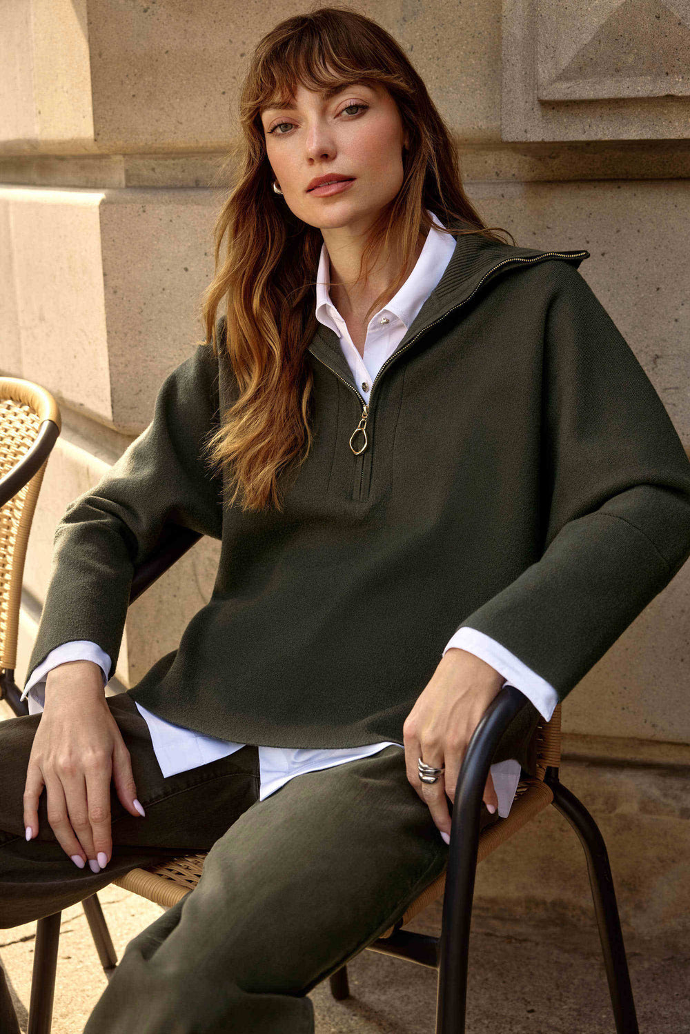 Woman wearing a green sweater and white shirt sitting outdoors.