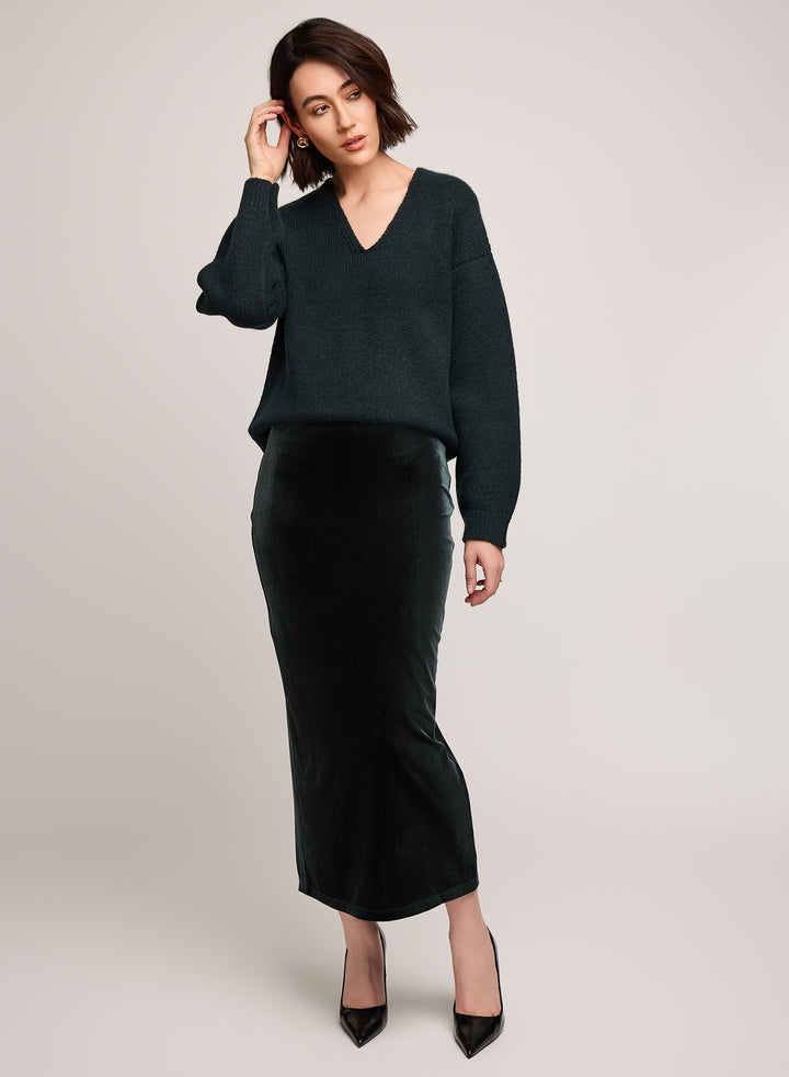 Woman wearing a dark green sweater and velvet skirt on a light background