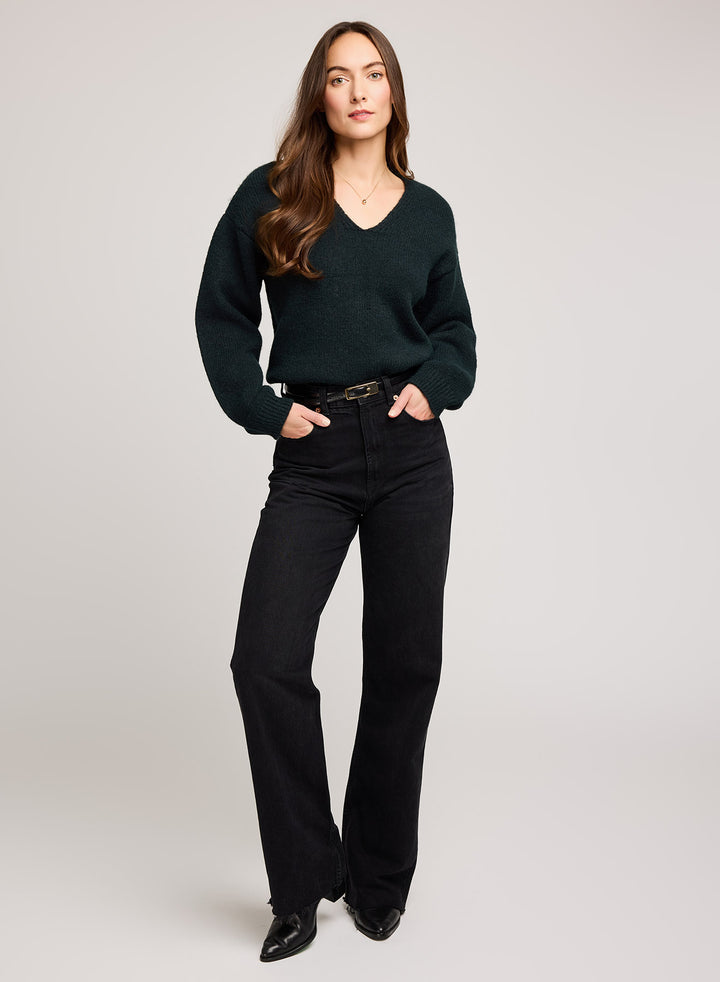 Woman wearing a dark green sweater and black pants on a light gray background