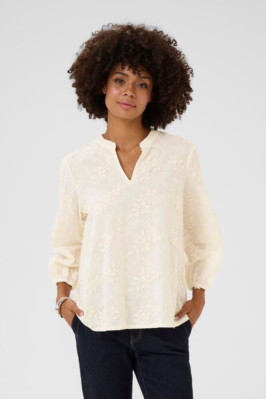 Woman wearing a cream blouse with a subtle pattern on a plain background