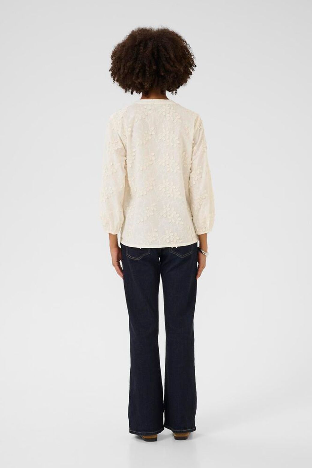 Person wearing a cream sweater and dark pants on a white background